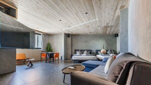 Ein modernes Hotelzimmer mit Holzbalkendecke, einem großen Bett, einer Sitzecke, einem kleinen Tisch und einem Essbereich mit Stühlen.