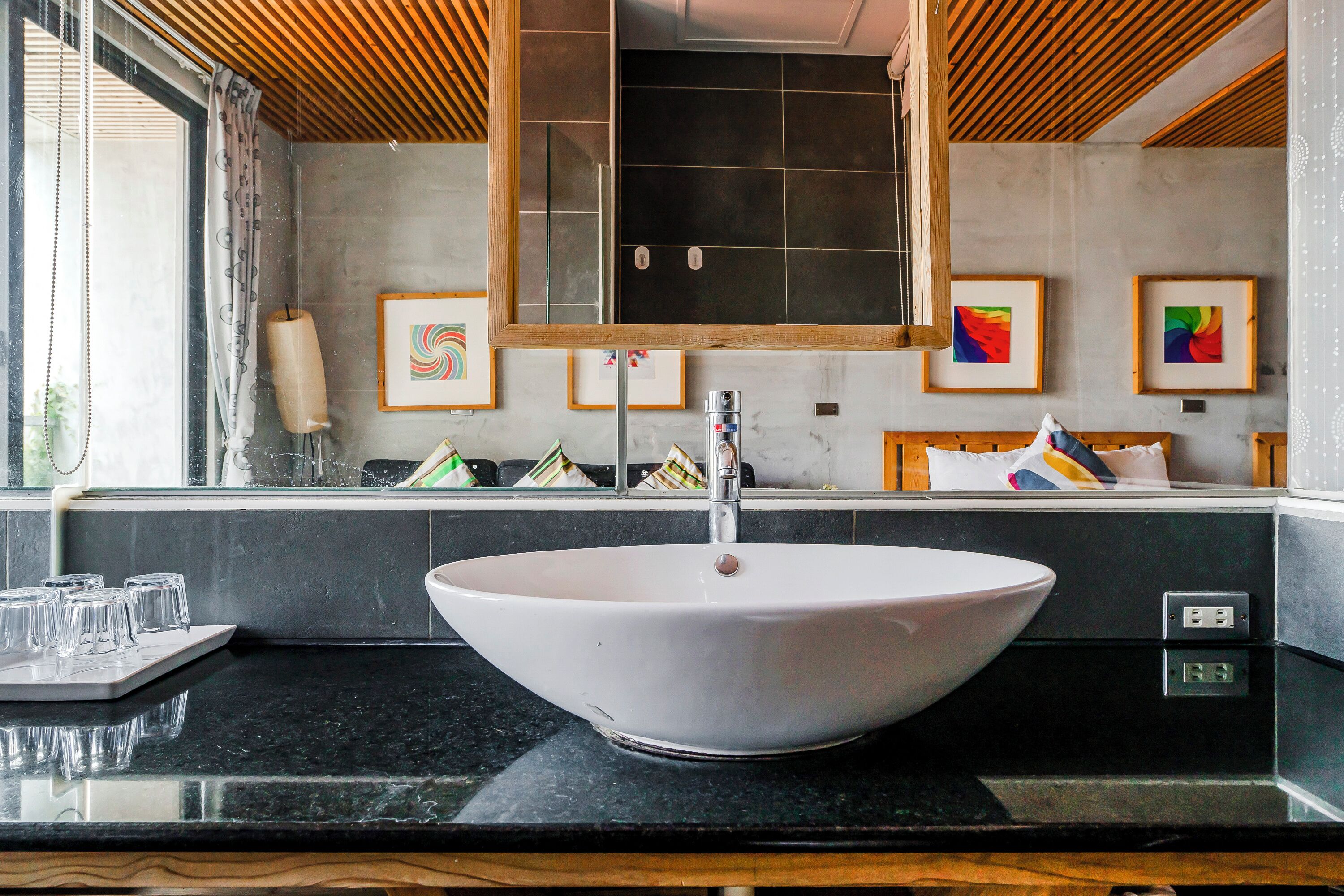 A modern bathroom with a large oval sink, a mirror, and framed artwork on the wall.