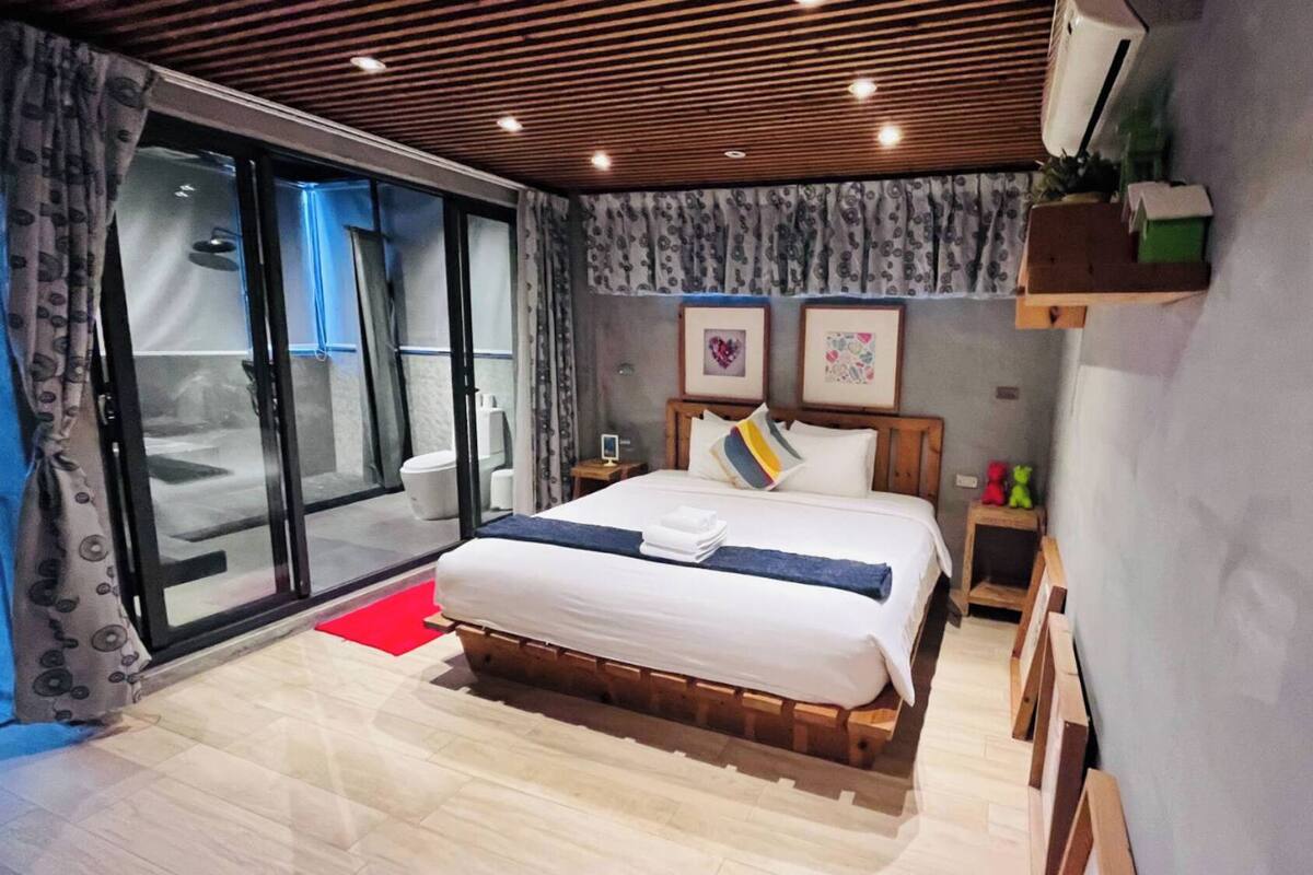 A bedroom with a large bed, a sliding glass door to a balcony, and a small bedside table with a lamp.