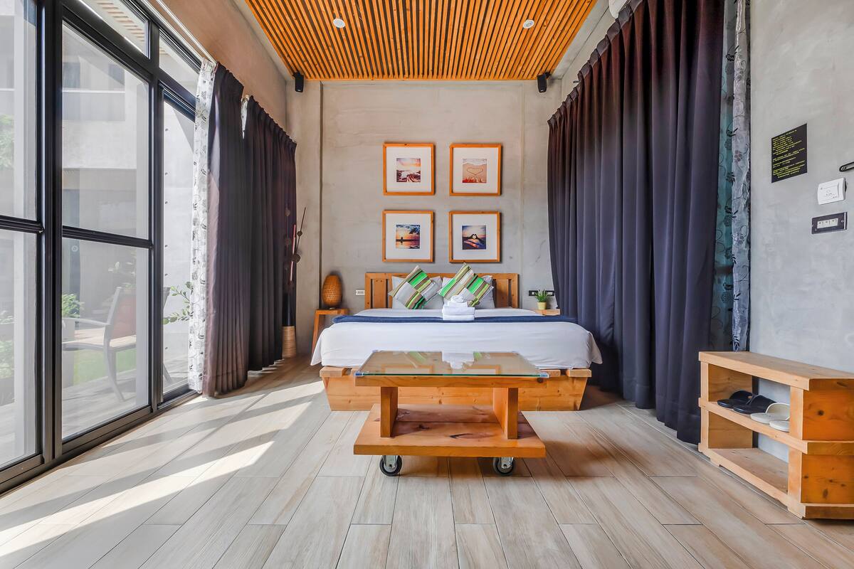 A modern bedroom with a large bed, a wooden nightstand, a bedside table, and a view through large windows.