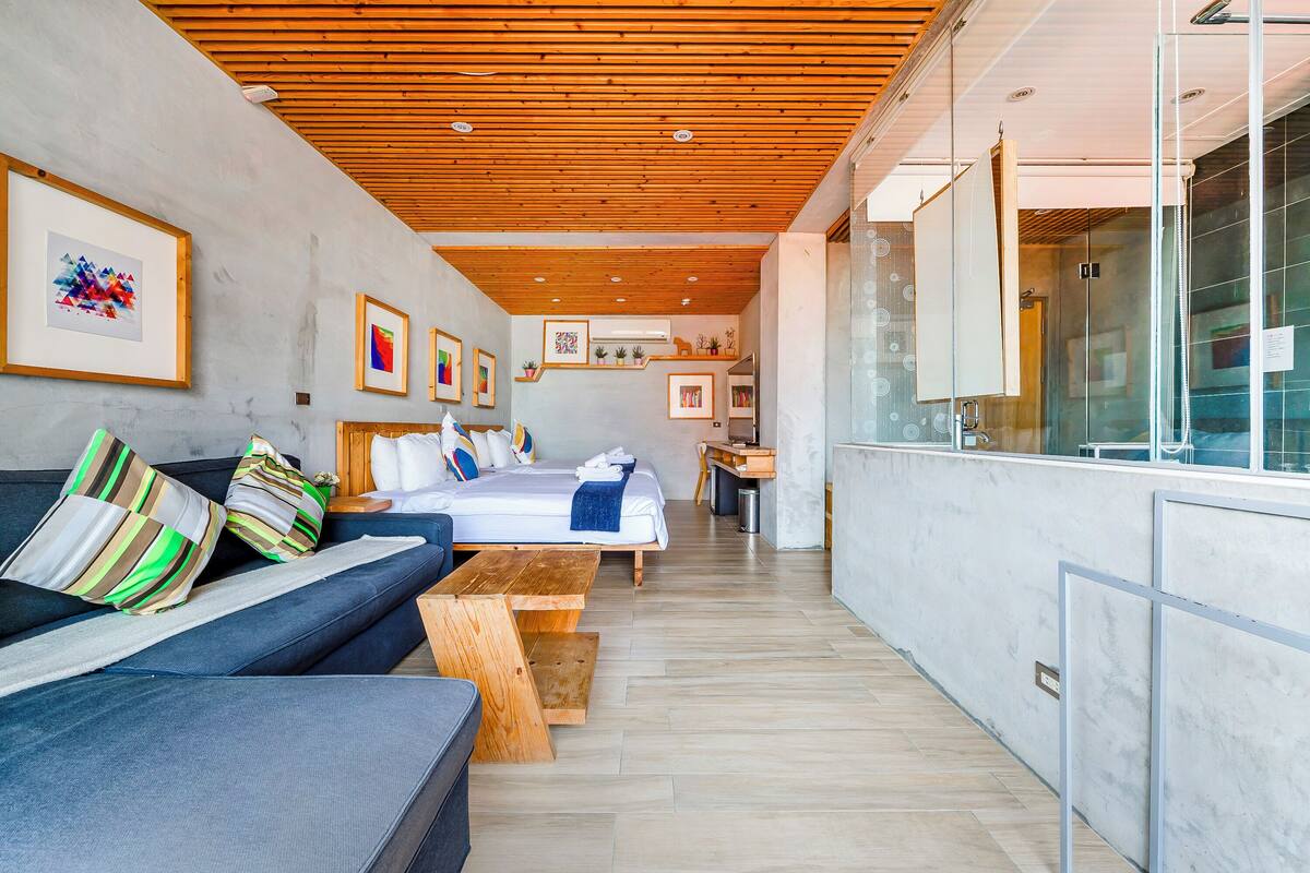 A modern hotel room with a wooden ceiling, a sofa, a bed, and a dining area.