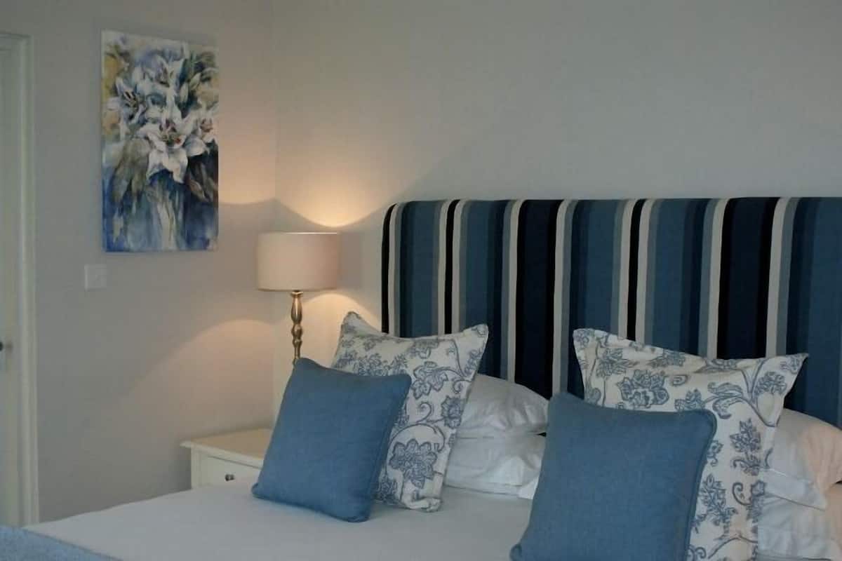 A bedroom with a bed, pillows, a bedside table, a lamp, and a painting on the wall.