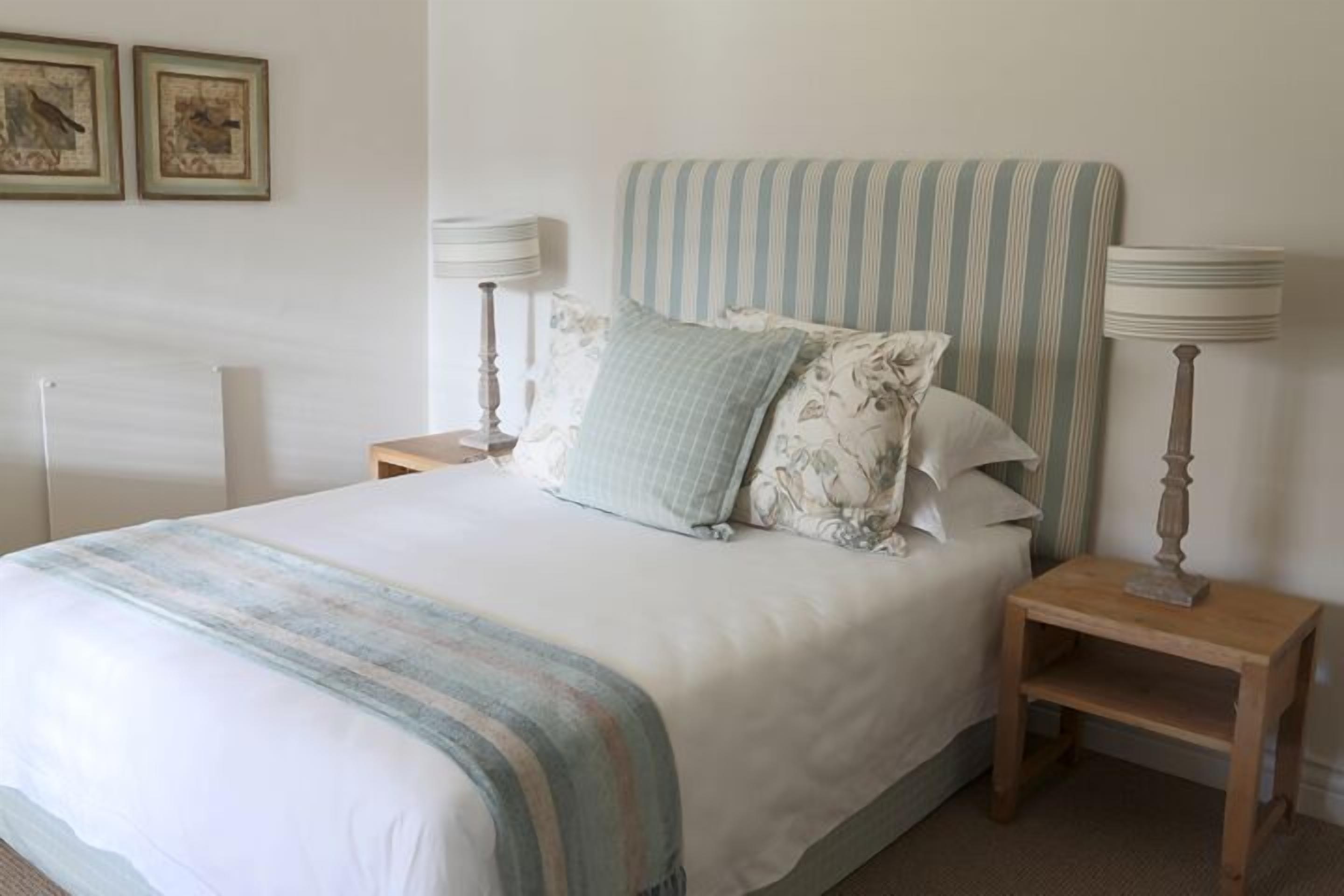 A neatly made bed with striped bedding, two bedside lamps, and two framed pictures on the wall.