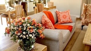 A living room with a sofa, a coffee table with a floral arrangement, and a dining area in the background. - Kingsmead Guest House (Harare)