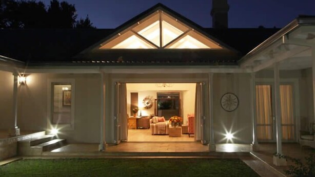 A house with a covered porch, a visible living room with a sofa and a coffee table, and a clock on the wall. - Kingsmead Guest House (Harare)