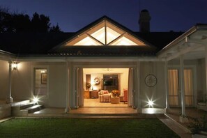 A house with a covered porch, a visible living room with a sofa and a coffee table, and a clock on the wall. - Kingsmead Guest House (Harare)
