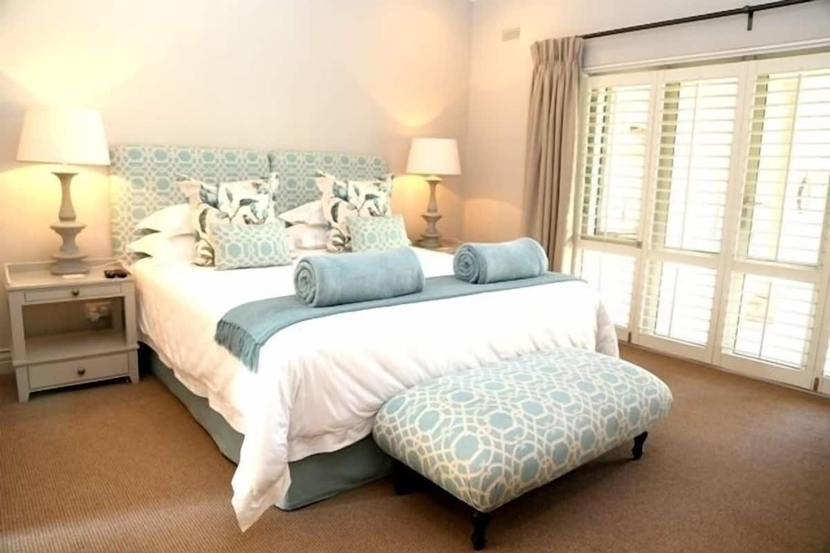 A bedroom with a bed, two bedside tables, a window with curtains, and a carpeted floor.