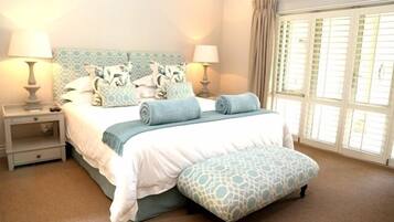 A bedroom with a bed, two bedside tables, a window with curtains, and a carpeted floor.