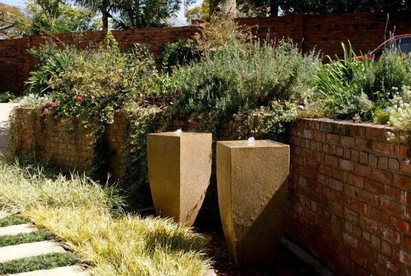 A garden area with two large stone planters, a brick wall, and various plants. - Kingsmead Guest House (Harare)