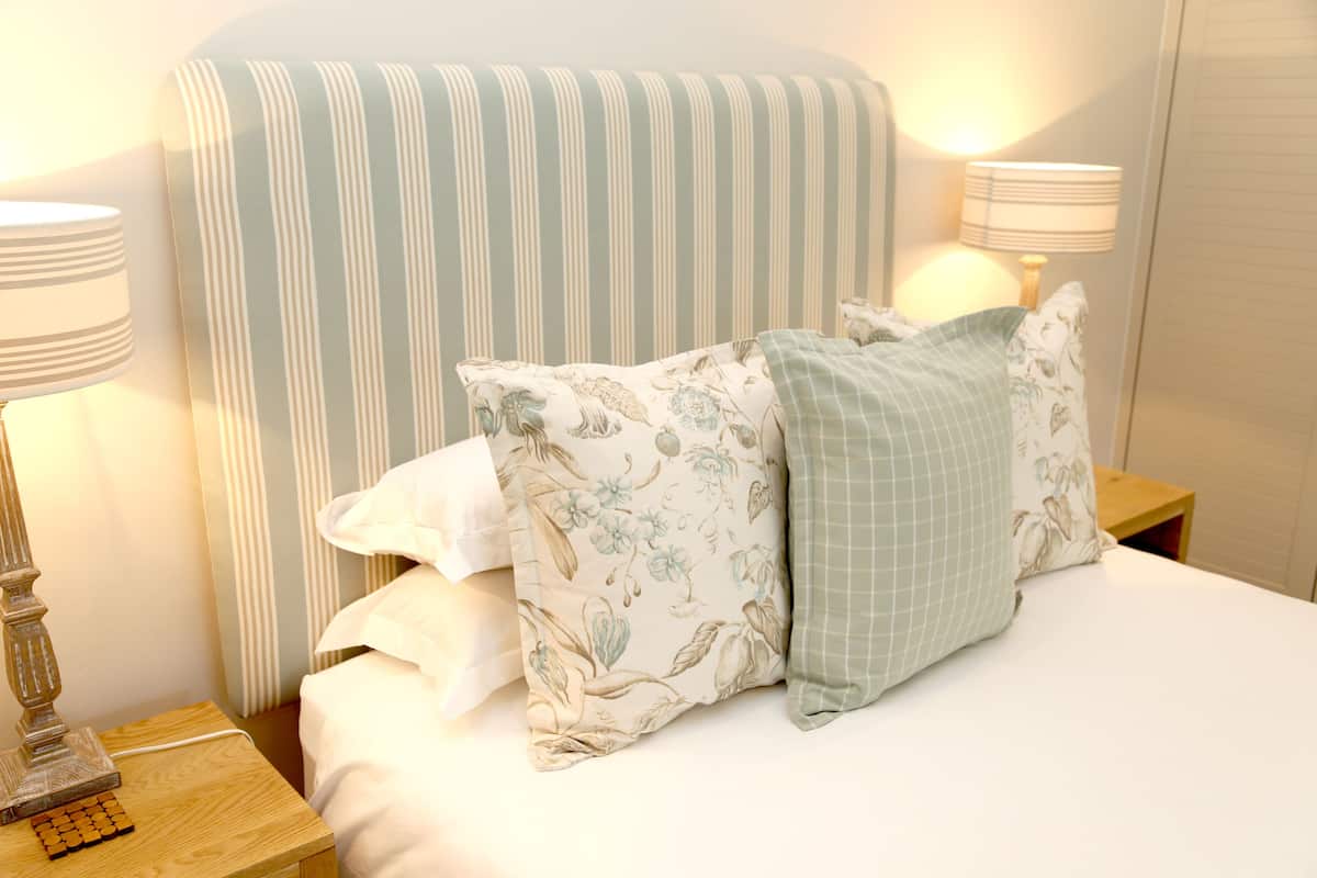 A neatly made bed with striped headboard, floral and checkered pillows, and bedside lamps on wooden nightstands.