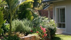 A house with a brick wall, lush garden, and a window. - Kingsmead Guest House (Harare)