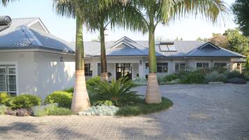 A two-story house with a paved driveway, palm trees, and a variety of plants.