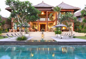 A resort with a pool, lounge chairs, and a large building with a thatched roof. - Villa Melissa (Munggu)