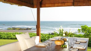 Une table dressée pour le dîner, avec vue sur l’océan, un toit de chaume et une structure en bois.