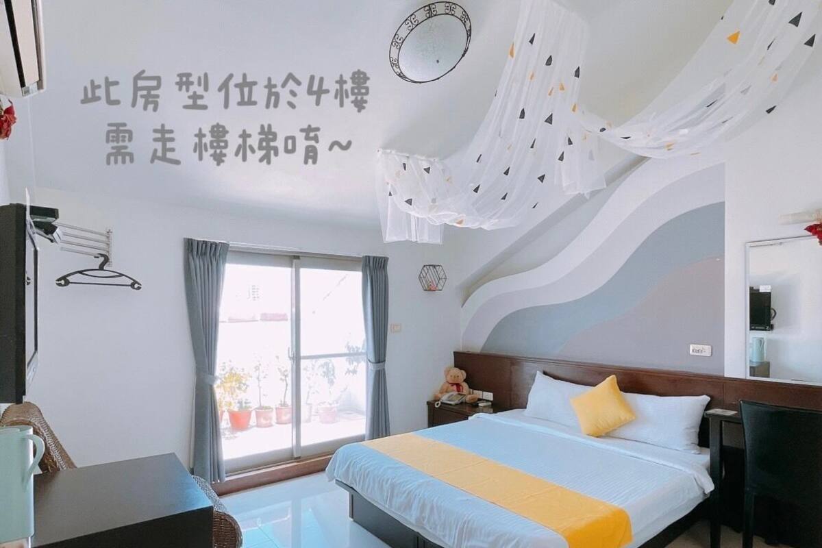 Ein Hotelzimmer mit Bett, Nachttisch, Stuhl, Schreibtisch, Fenster mit Vorhängen und einer Wand mit einer Dekoration.