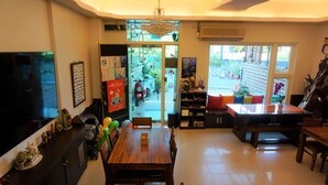 A spacious living area with a wooden dining table, a TV on the left, and a large window providing a view of the outdoors. - Warner Leisure Hotel (Hengchun)