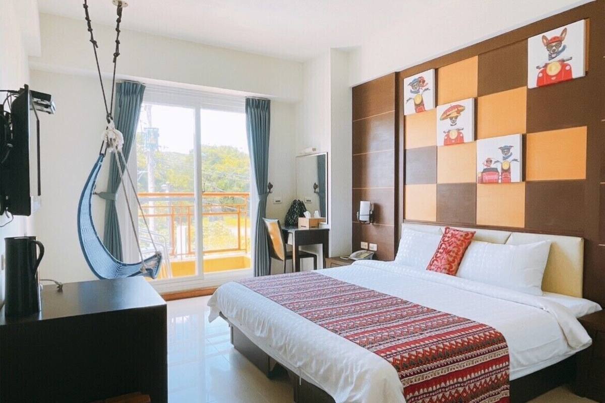 Ein Hotelzimmer mit einem großen Bett, einem Schreibtisch, einem Stuhl, einer Hängematte und einem Balkon mit Blick.