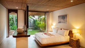 Ein Schlafzimmer mit einem großen Bett, Nachttischlampen, einem Holennachtschränkchen und Blick auf einen üppigen Garten.