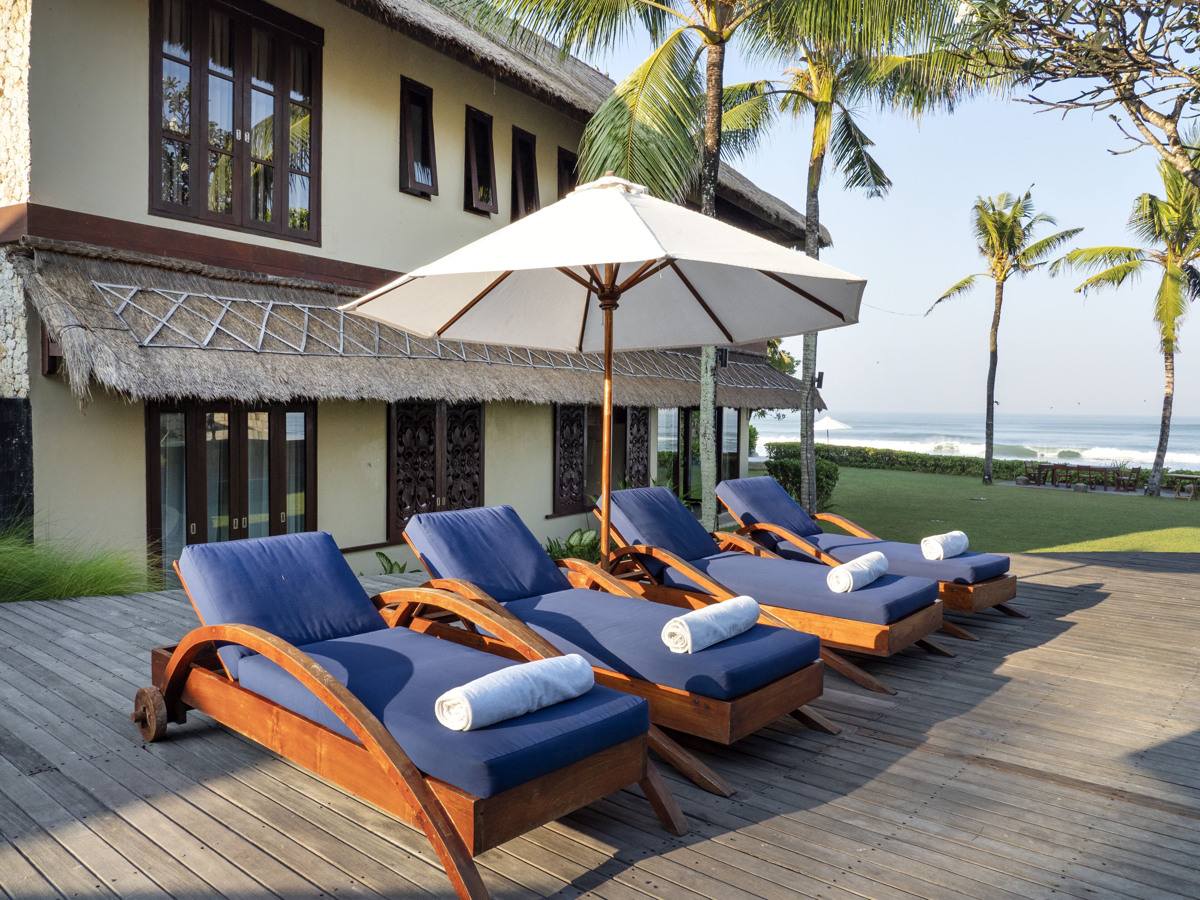 Een houten terras met lounge stoelen en een grote parasol, met uitzicht op een strand en de oceaan.