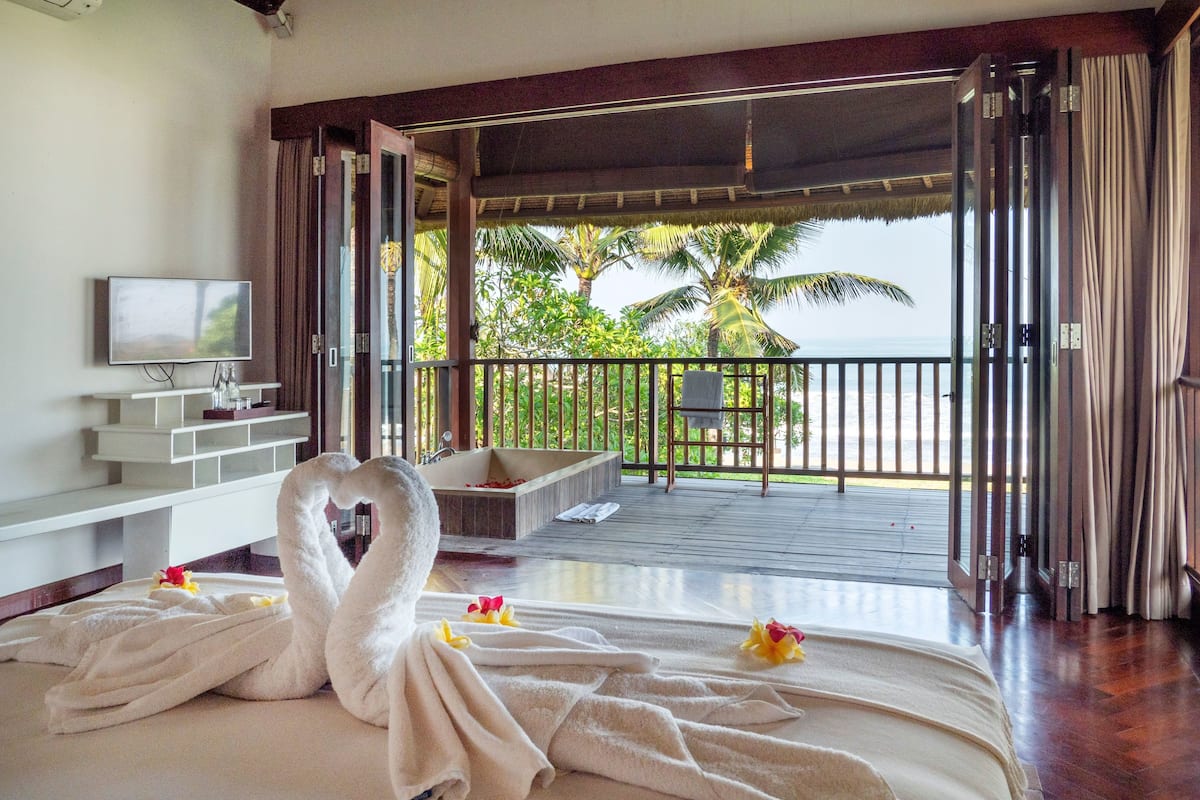 A bedroom with a bed, a TV, and a balcony with a view of the ocean.