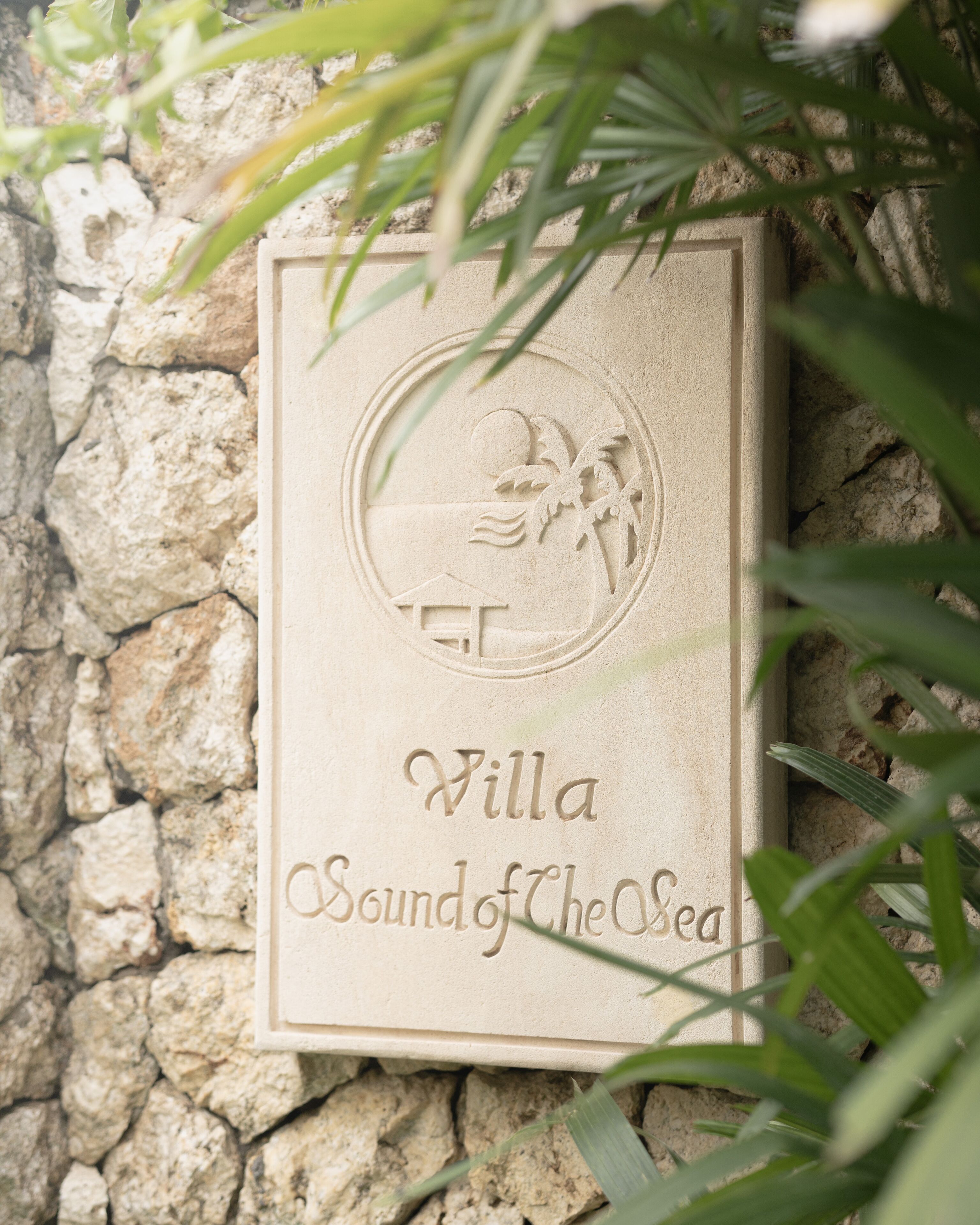 A stone plaque with the inscription "Villa Sound of the Sea" and a circular emblem featuring a palm tree and waves.