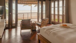 Ein Hotelzimmer mit einem Bett, einem Schreibtisch und einem Stuhl. Das Zimmer verfügt über große Fenster mit Blick auf den Strand und das Meer.