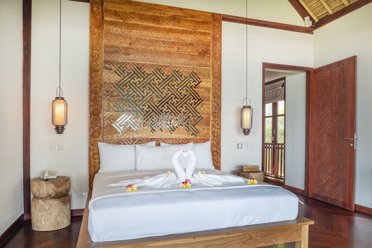 A spacious bedroom with a large bed, wooden headboard, and two wall-mounted lamps.