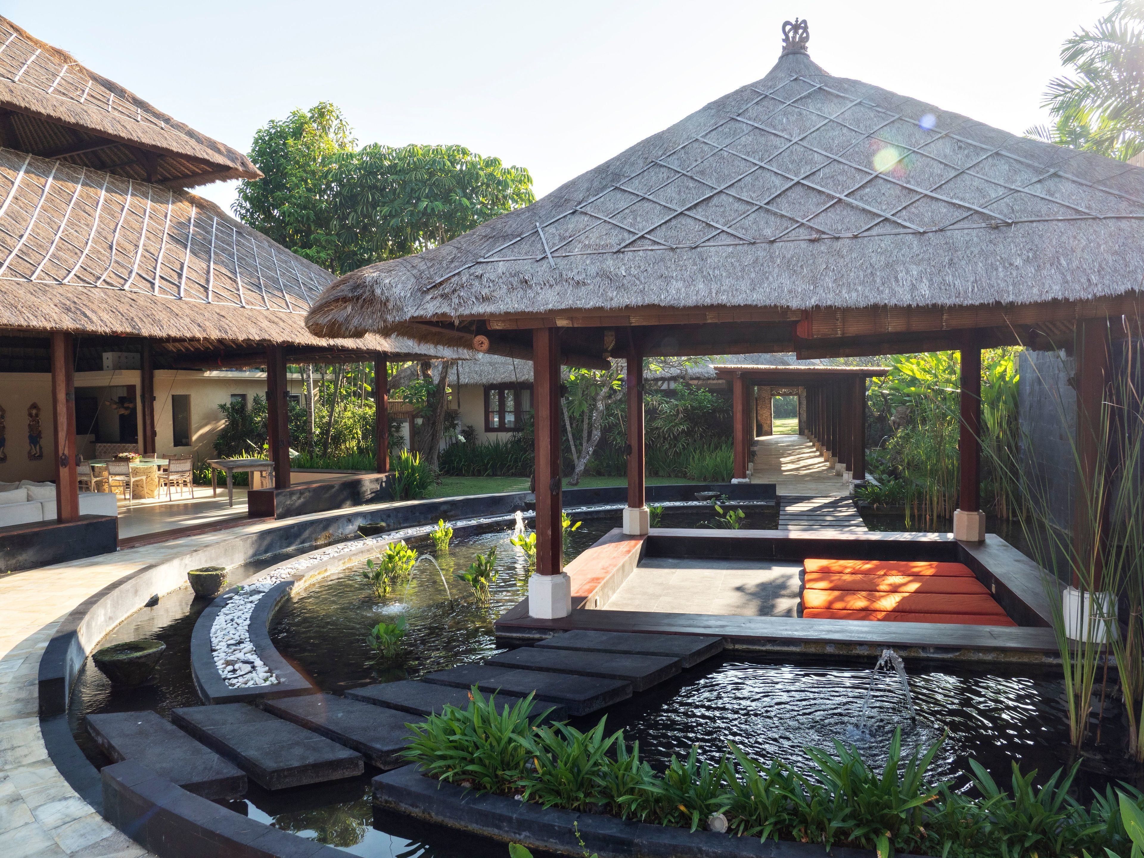 A traditional thatched-roof pavilion with a water feature in the center, surrounded by stone steps and greenery.