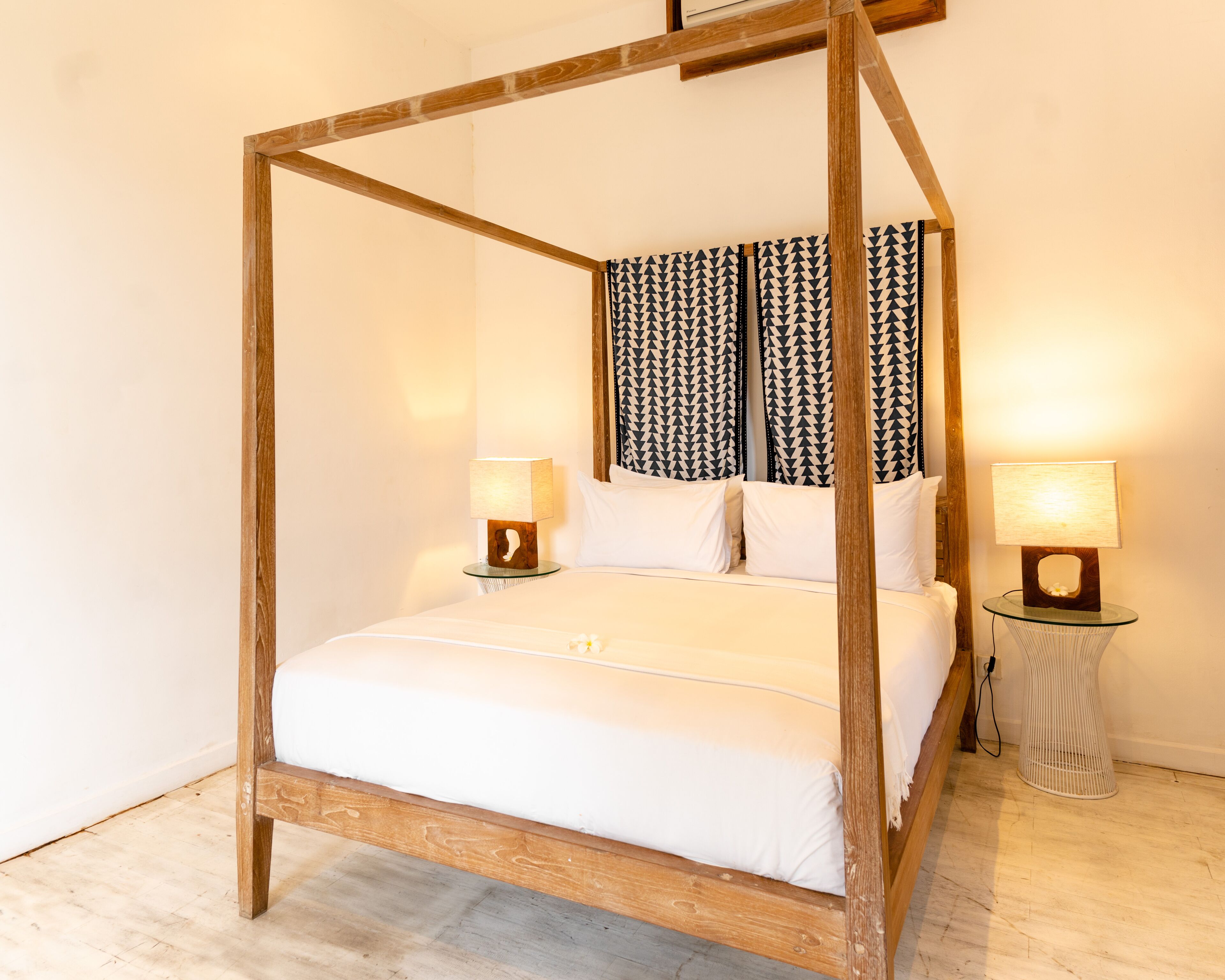 Ein Bett mit Baldachin, ausgestattet mit weißen Bettwäsche, zwei Nachttische mit Lampen und gemusterten Vorhängen.