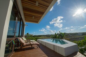 Relax by the pool surrounded by lush greenery and enjoy the comfort of lounge chairs and a small table.