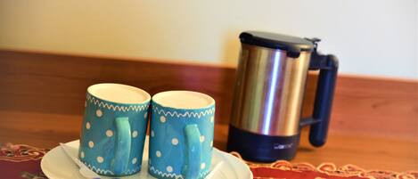 Two polka-dotted mugs on a plate with a thermos and some packets on a table with a patterned tablecloth.