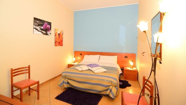 A bedroom with a bed, two chairs, a nightstand, a lamp, and wall art. - B&B Dimora dell'Etna (Milo)