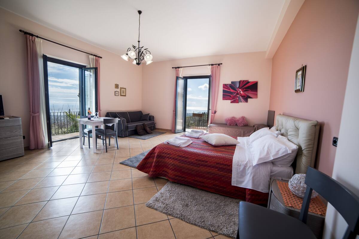 Un dormitorio con cama, escritorio, sofá y vistas al exterior.