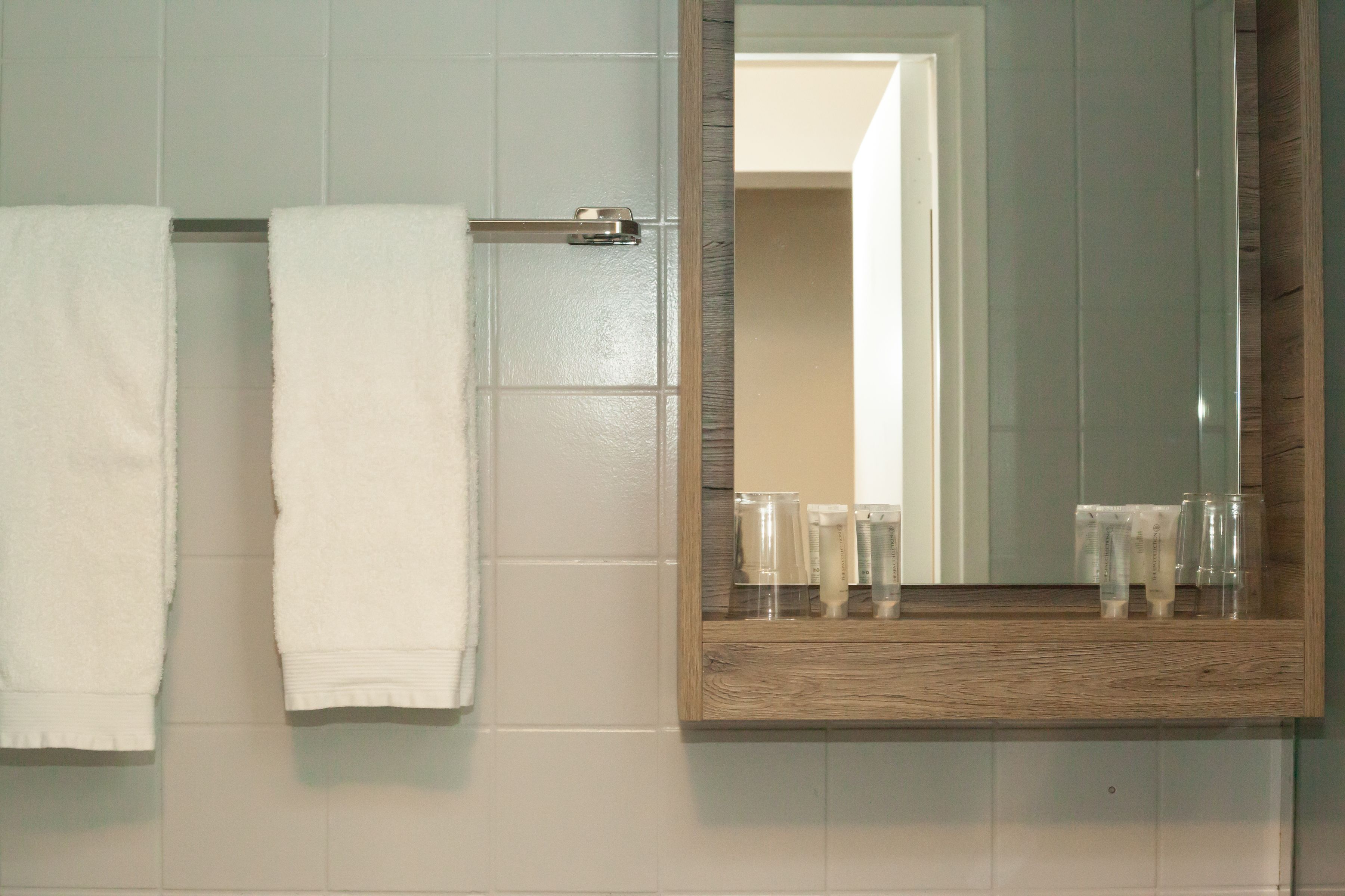 Un baño con un espejo de marco de madera, azulejos blancos y dos toallas blancas colgadas en un perchero.