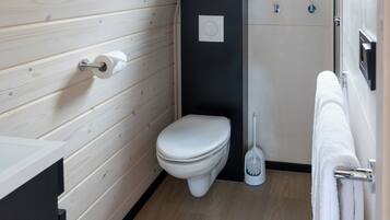 A compact, modern bathroom with a wooden wall, a white toilet, a black cabinet, and a small window.