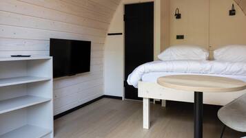 Un dormitorio moderno con cama, una mesa redonda, televisor en un estante y una puerta.