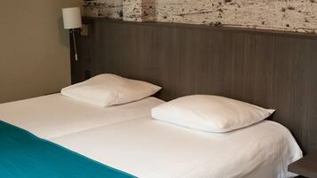 Habitación de hotel con cama, dos almohadas, una manta color aguamarina, una lámpara de pared y una pared texturizada sobre la cama.