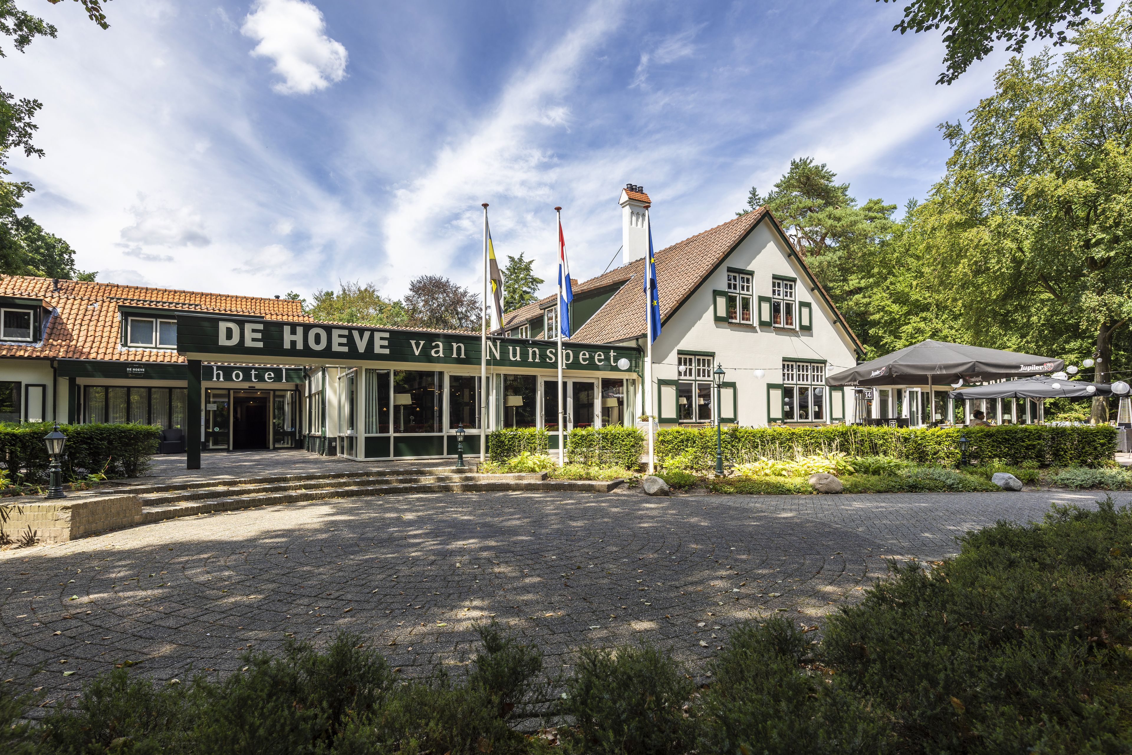 Een hotel in traditionele Europese bouwstijl, met een opvallende ingang, een pannendak en een verzorgde tuin.