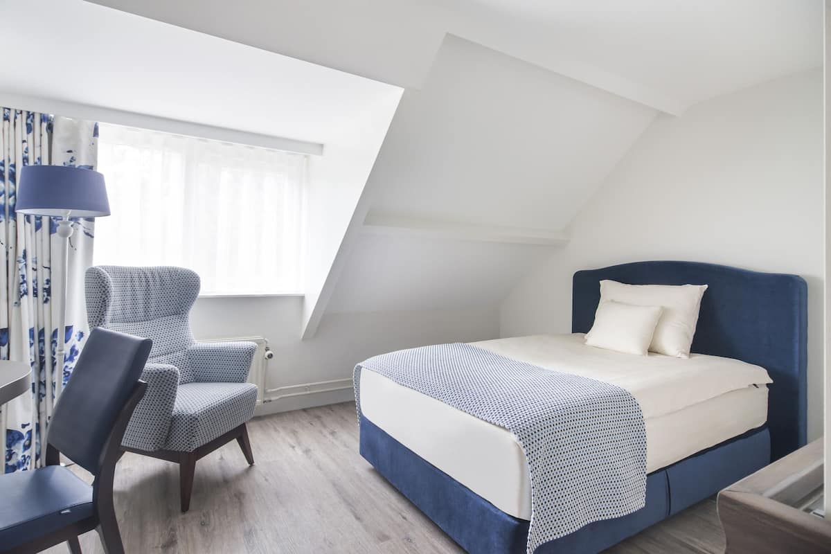 Un dormitorio con cama, una silla, un escritorio y una ventana con cortinas.