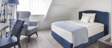 Un dormitorio con cama, una silla, un escritorio y una ventana con cortinas.
