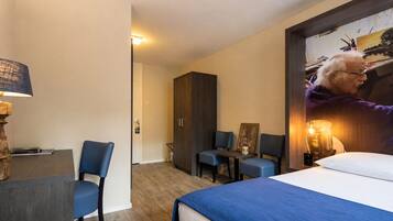 Habitación de hotel con cama, escritorio, dos sillas, armario y un cuadro en la pared.