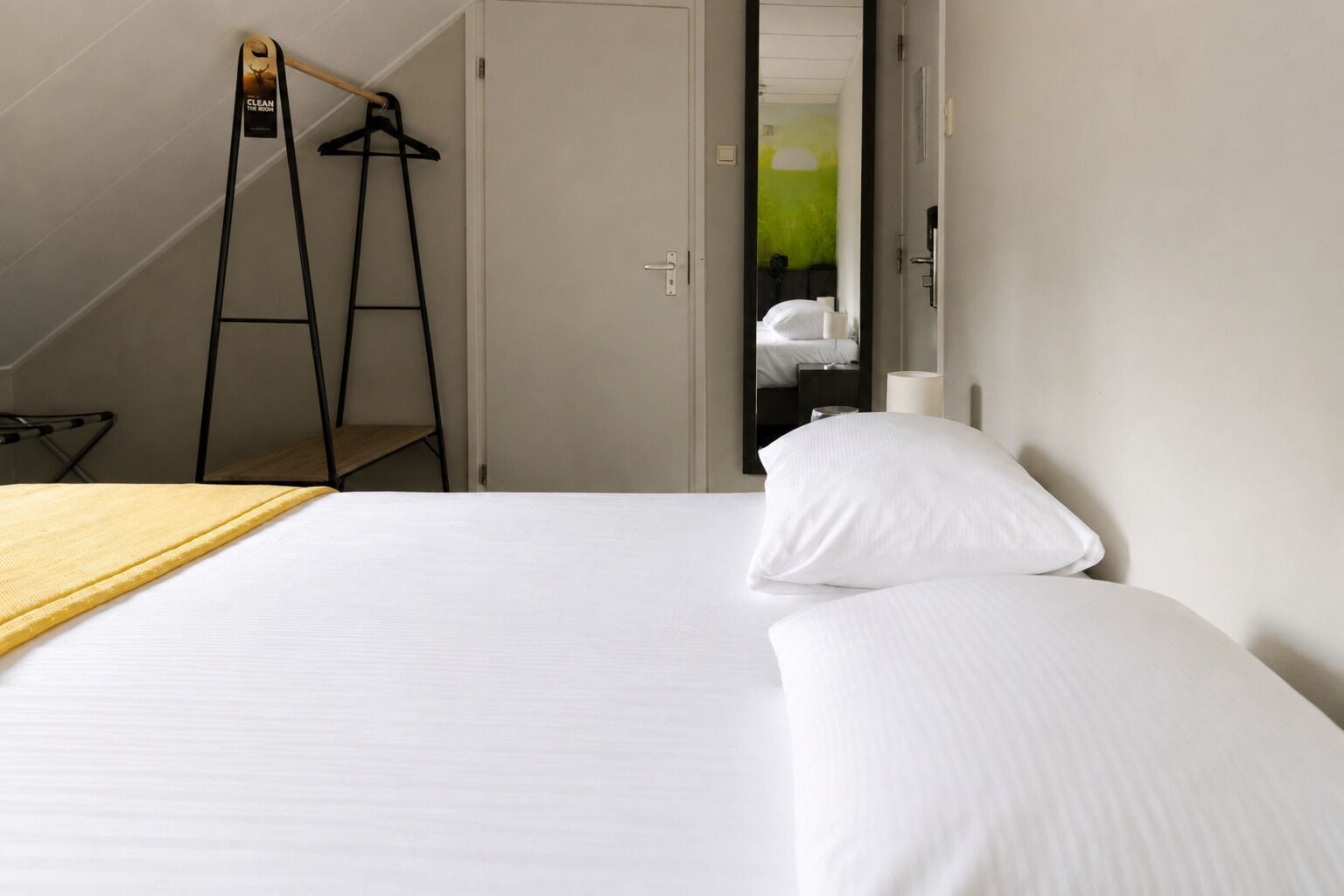 A hotel room with a bed, a wooden ladder, and a coat rack.