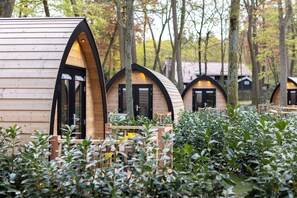 A row of wooden cabins with arched doorways, surrounded by dense foliage. - Hotel De Hoeve van Nunspeet (Nunspeet)