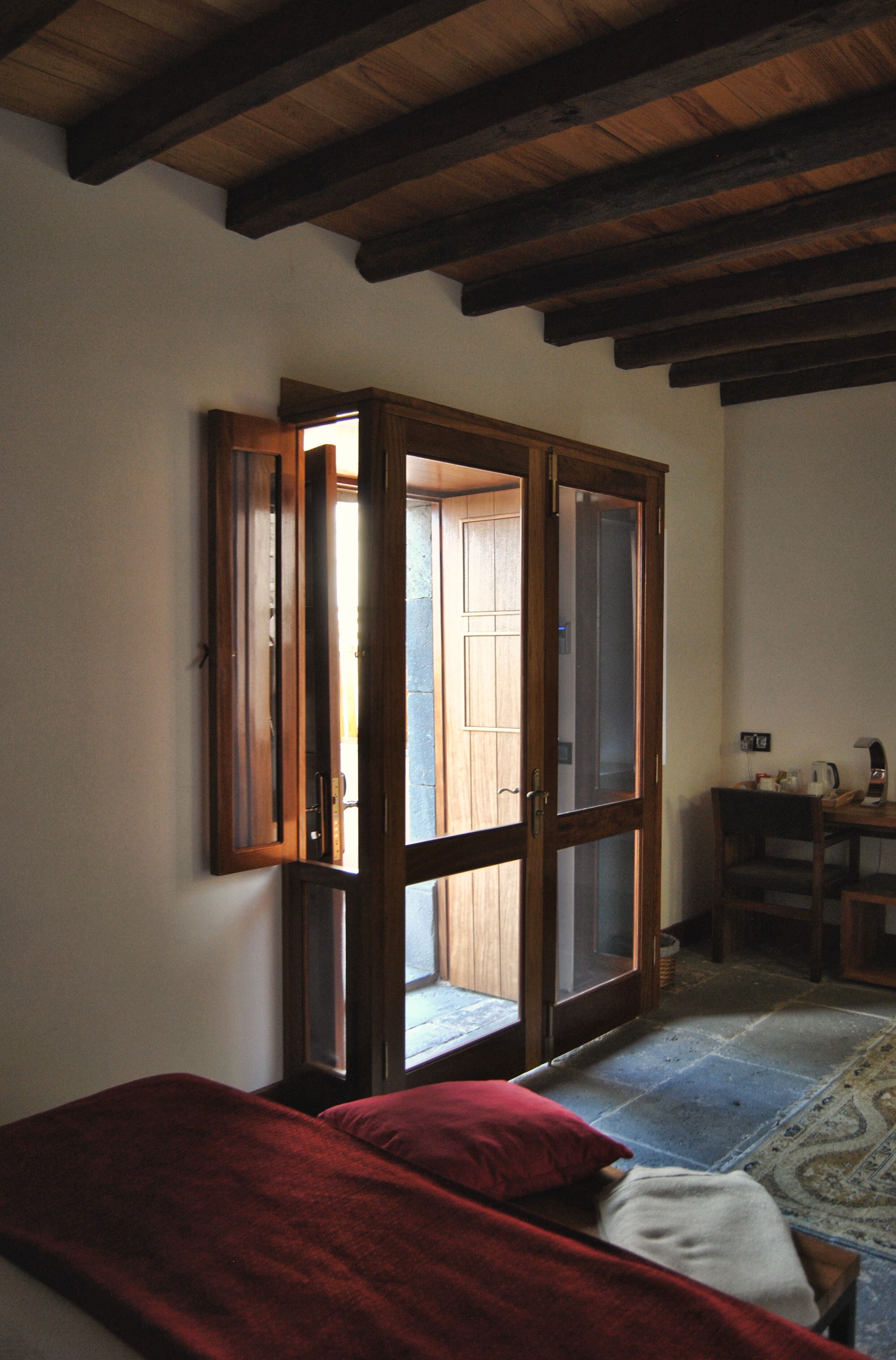 Una habitación con una cama, un armario de madera con puertas de cristal, un escritorio con una silla y un tapete estampado en el suelo.