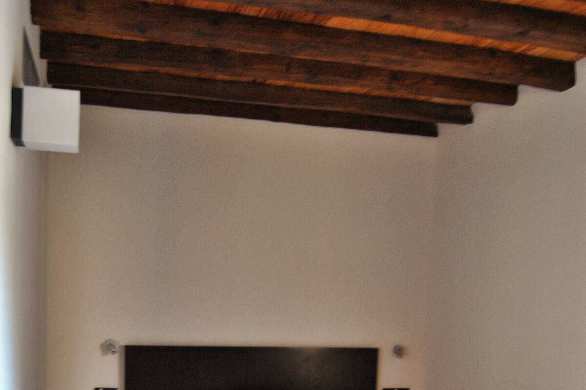 Een slaapkamer met een bed, nachtkastje, een bankje en een houten plafond.