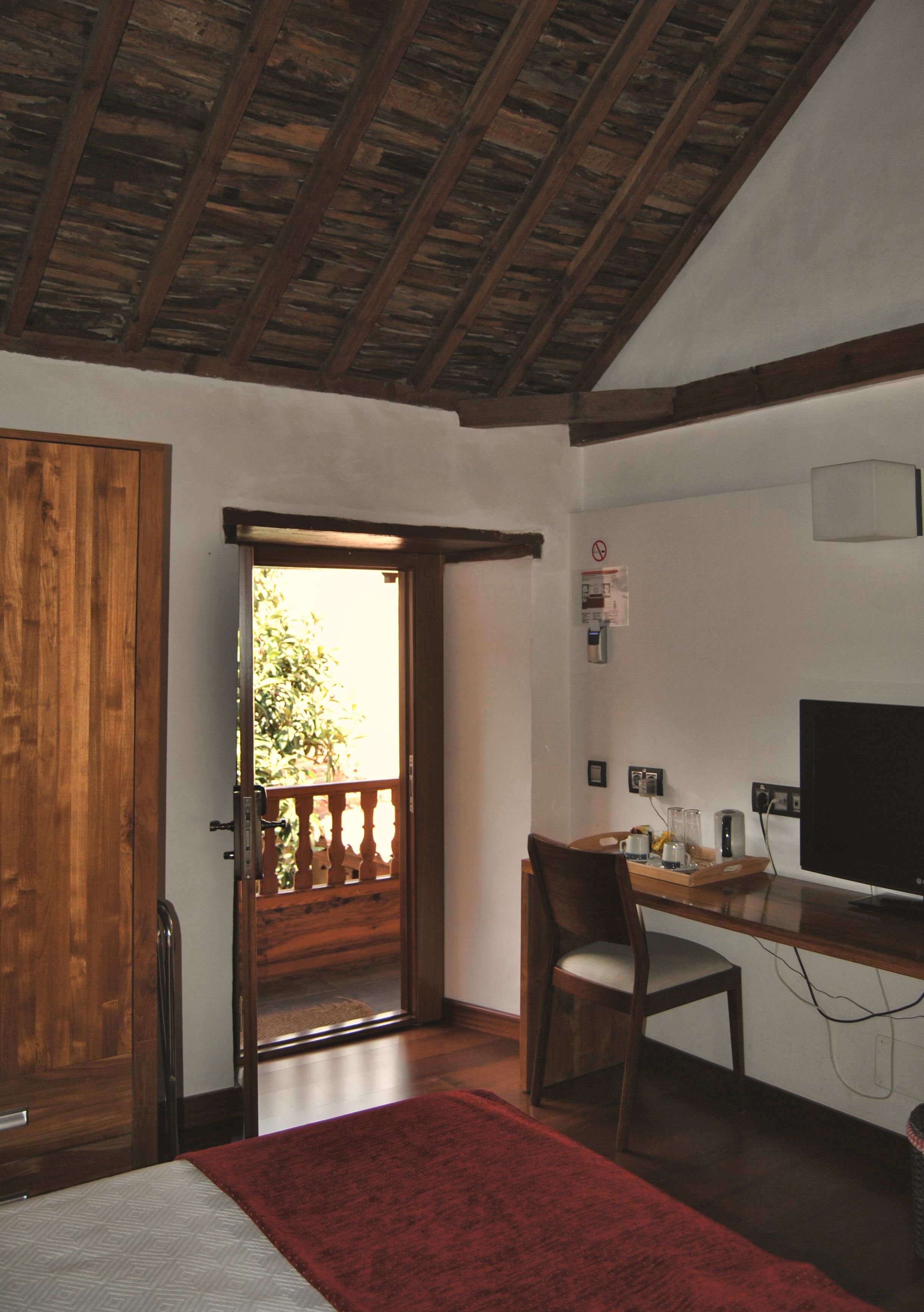 A room with a wooden door, a desk with a computer, a chair, and a red rug.