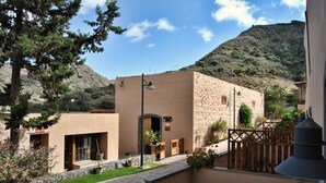 A courtyard with a stone building, a wooden fence, and a mountain in the background. - Hotel Rural El Mondalón (Las Palmas de Gran Canaria)