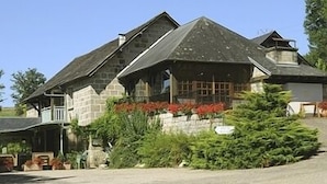 A stone building with a gabled roof, a porch, and a well-maintained garden with various plants and a Christmas tree. - Le Domaine de Renaudet (Saint-Pantaleon-de-Larche)