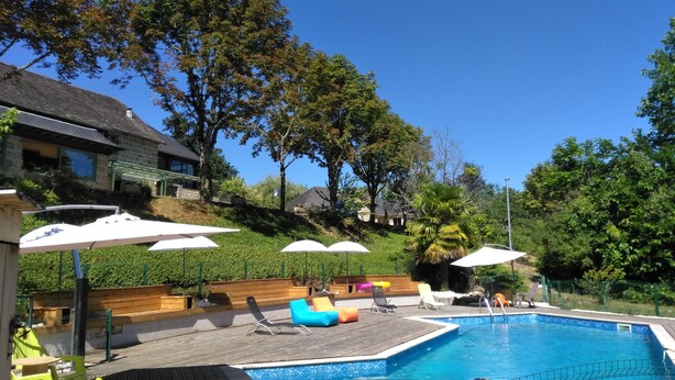 A swimming pool with lounge chairs and umbrellas, surrounded by trees and a house in the background. - Le Domaine de Renaudet (Saint-Pantaleon-de-Larche)