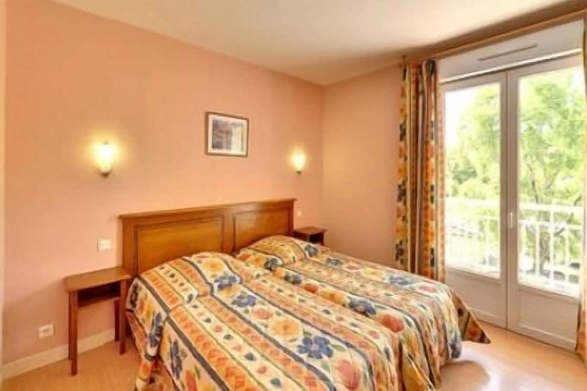 A bedroom with a bed, a nightstand, two wall sconces, a framed picture, and a sliding glass door leading to a balcony.